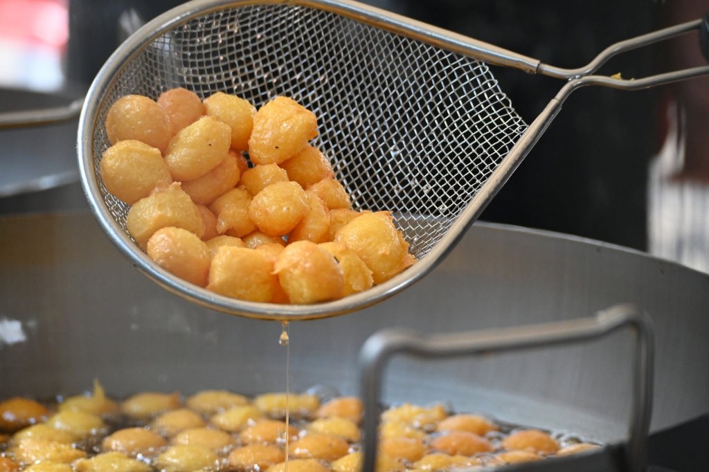 Una schiumarola solleva palline fritte dorate da una padella profonda con olio caldo.