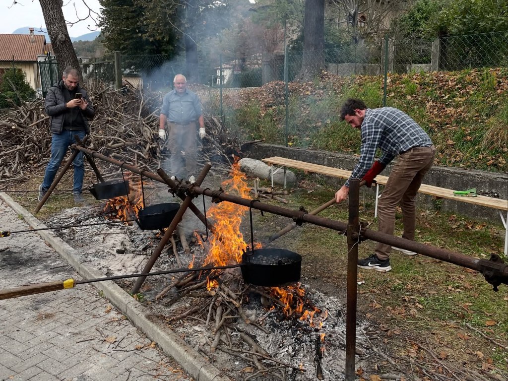 Tre uomini stanno cucinando su un fuoco all'aperto con pentole nere sospese sopra le fiamme.