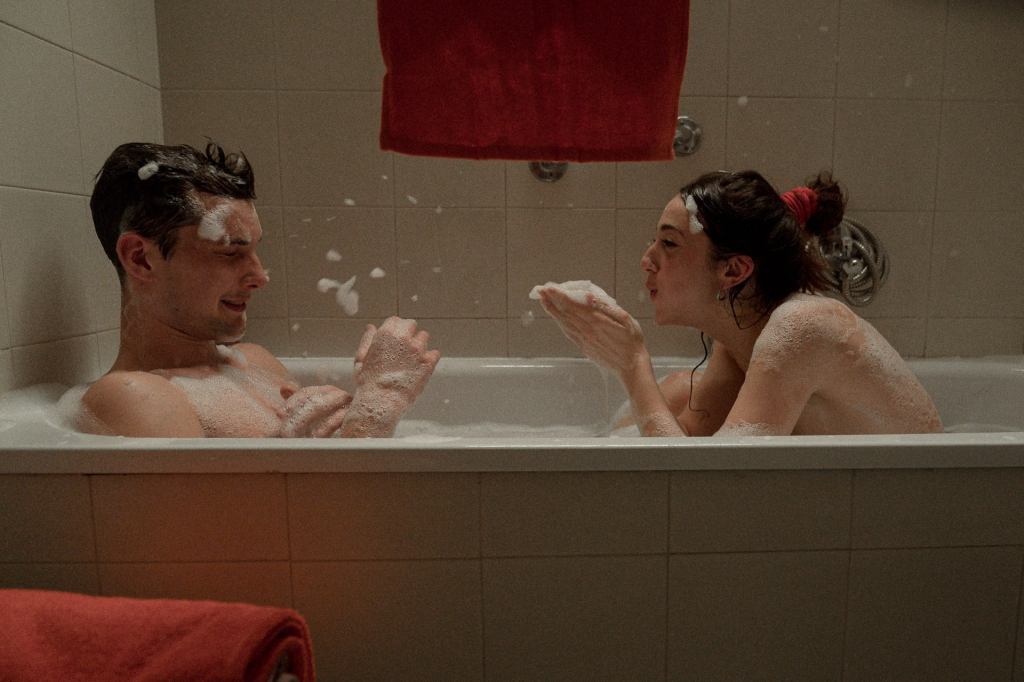 Due persone si divertono in una vasca da bagno piena di schiuma, con una atmosfera giocosa e rilassata.
