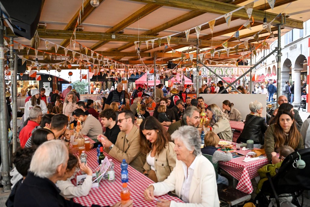 Una vivace fiera gastronomica all'aperto con tavoli affollati e persone che mangiano, sotto un tetto decorato con festoni.