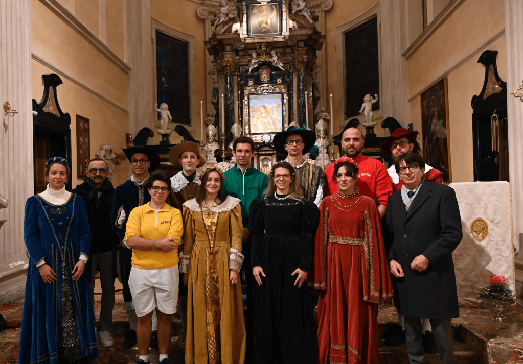 Un gruppo di persone in costumi storici all'interno di una chiesa, con decorazioni e un altare sullo sfondo.