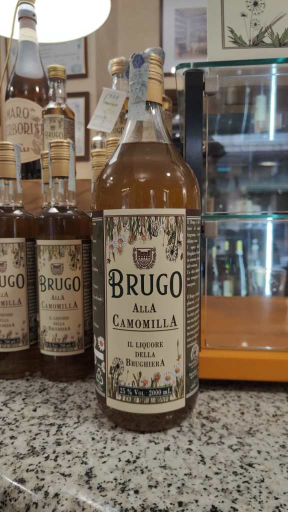 Bottiglia di liquore Brugo alla Camomilla, con etichetta chiara e dettagli floreali, esposta su un bancone di pietra.